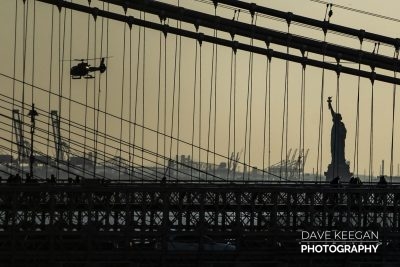 Statue of Liberty silhouette through The Brooklyn Bridge